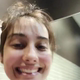 A very cute girl in a public restroom lowers her pants and sits on the toilet, filmed from below the seat. No poop action shown. Brief clip. Vertical format video. About half a minute.